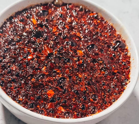 Close-up of spicy chili oil in a white bowl, vibrant red color and textured surface