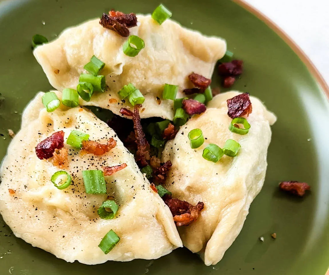 Pierogi dumplings topped with bacon and green onions on a green plate