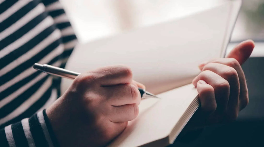 Person in striped shirt writing in blank notebook with pen, closeup, Mora balance theme.