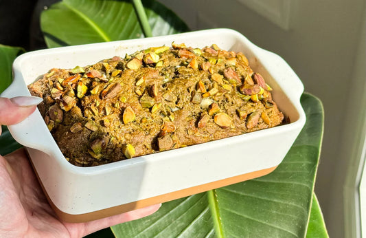 Freshly baked pistachio loaf in a ceramic dish, held above green leaves in natural light
