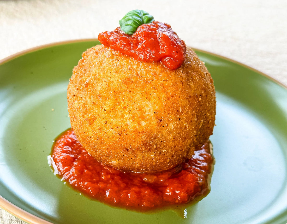 Crispy arancini with tomato sauce and basil on green plate, Mora restaurant presentation