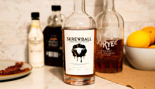 Skrewball peanut butter whiskey bottle on marble counter with spirits, syrup, and citrus bowl