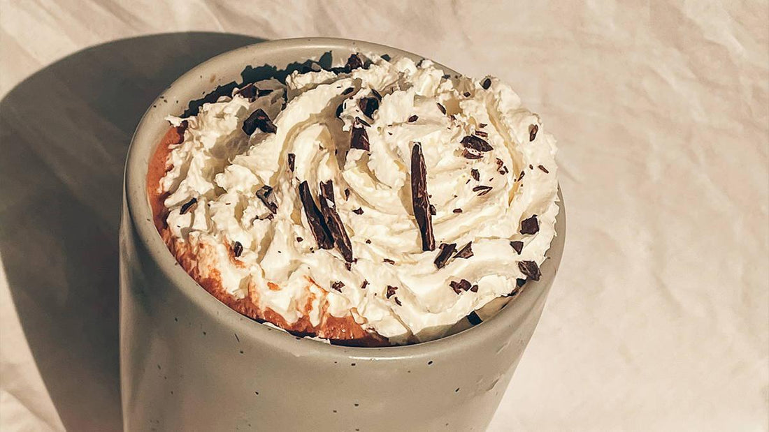 Ceramic mug of hot chocolate with whipped cream and chocolate shavings on white table
