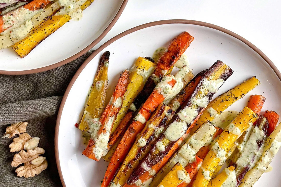Roasted rainbow carrots with herb sauce on Mora ceramic plate, walnuts on linen napkin nearby