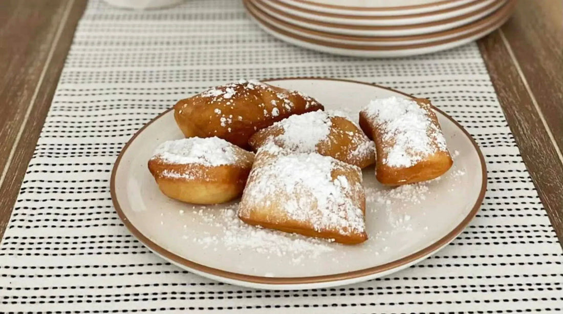 Powdered sugar beignets on a ceramic plate atop a striped table runner, Mora style