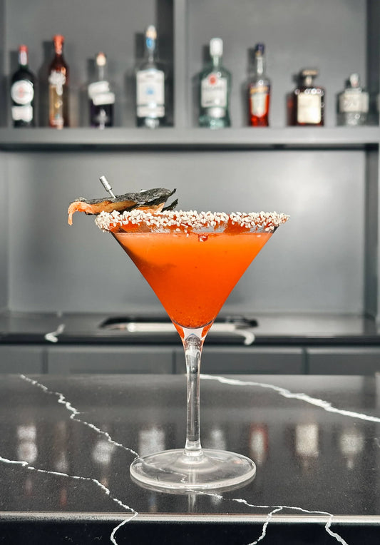 Elegant red cocktail in a martini glass with sesame rim, displayed on a black marble bar at Mora