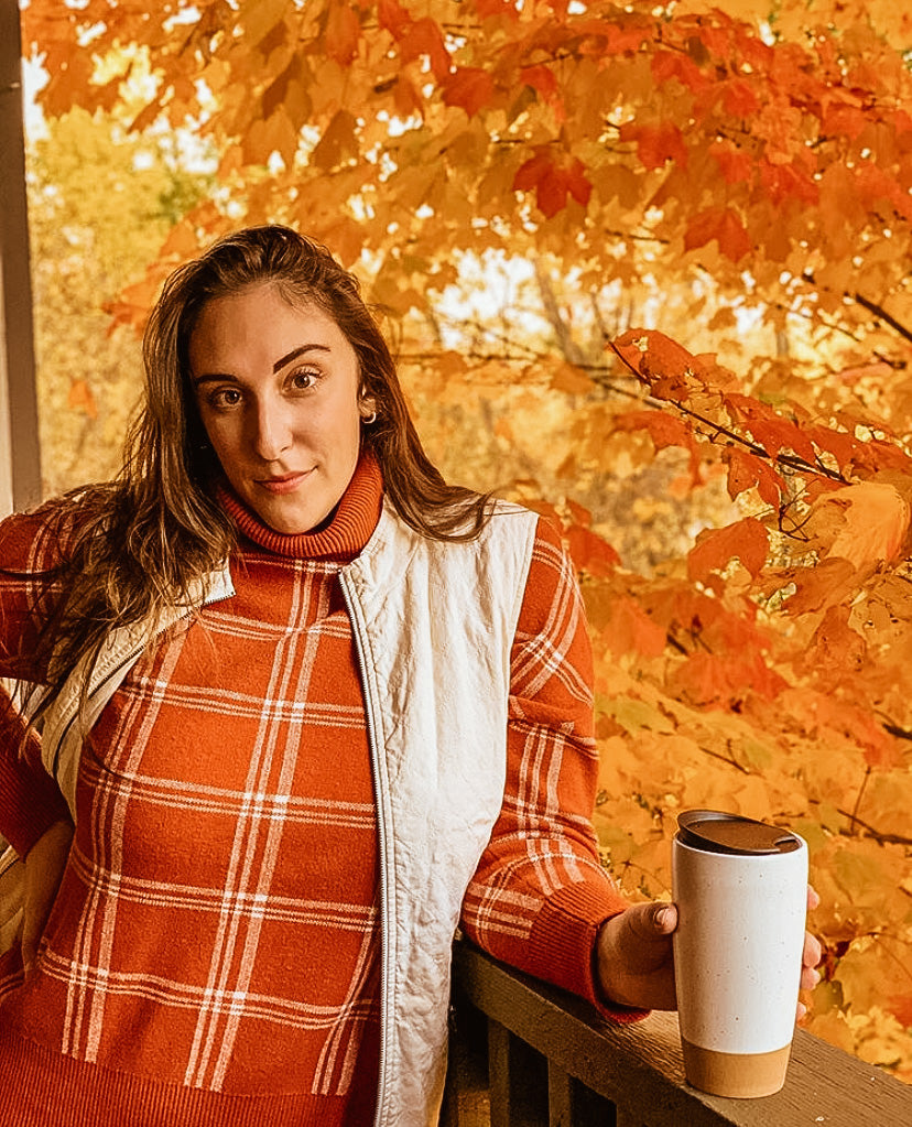instagram influencer holding a ceramic travel mug next to a tree with fall colors